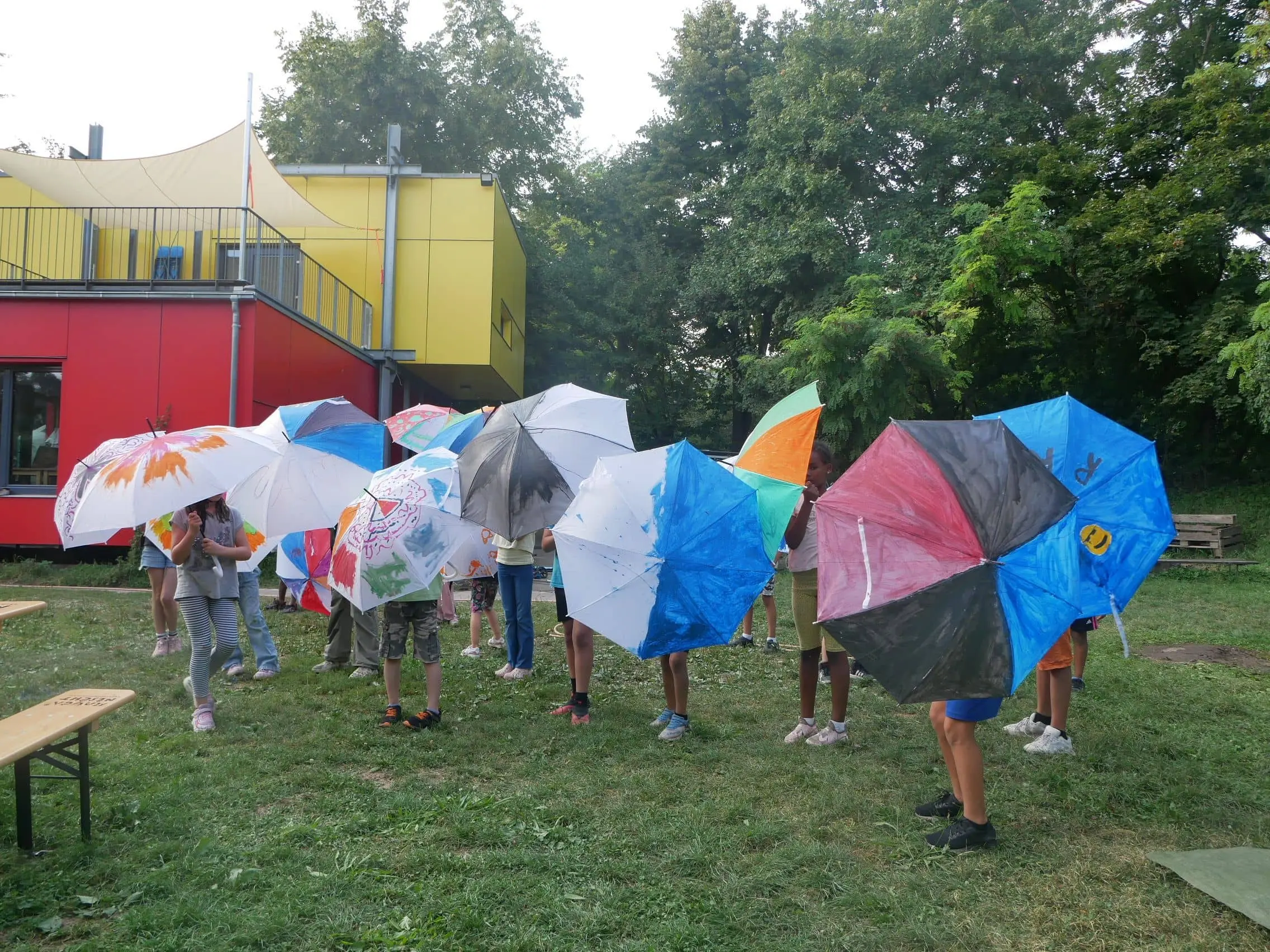 Kinder stehen auf einer Wiese und halten geöffnete Regenschirme in die Kamera, die bunt bemalt sind.
