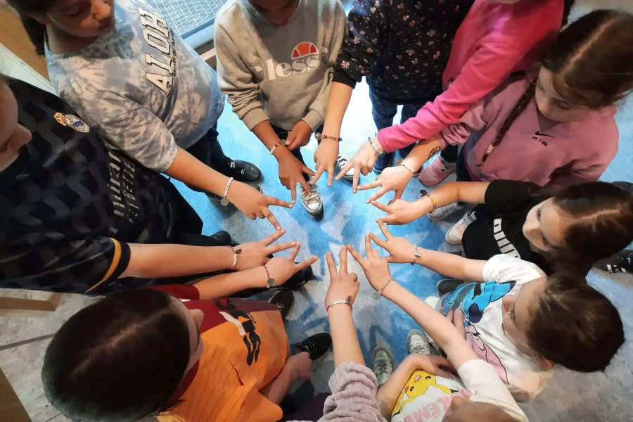 Kinder stehen eng zueinander im Kreis und bringen ihre Hände nach vorne zusammen, wie von oben zu sehen ist.
